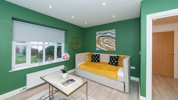 A room with a green wall, a sofa with a yellow blanket, a clock, and a painting.