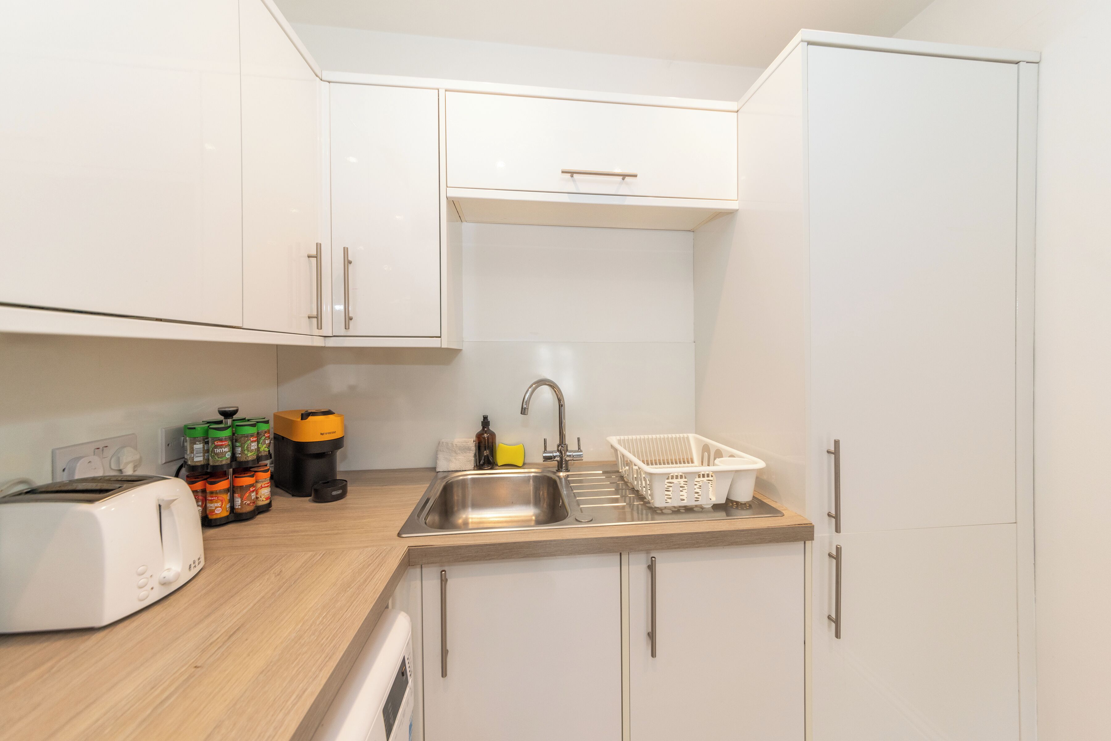 A kitchenette with a toaster, a sink, cabinets, and a coffee maker.