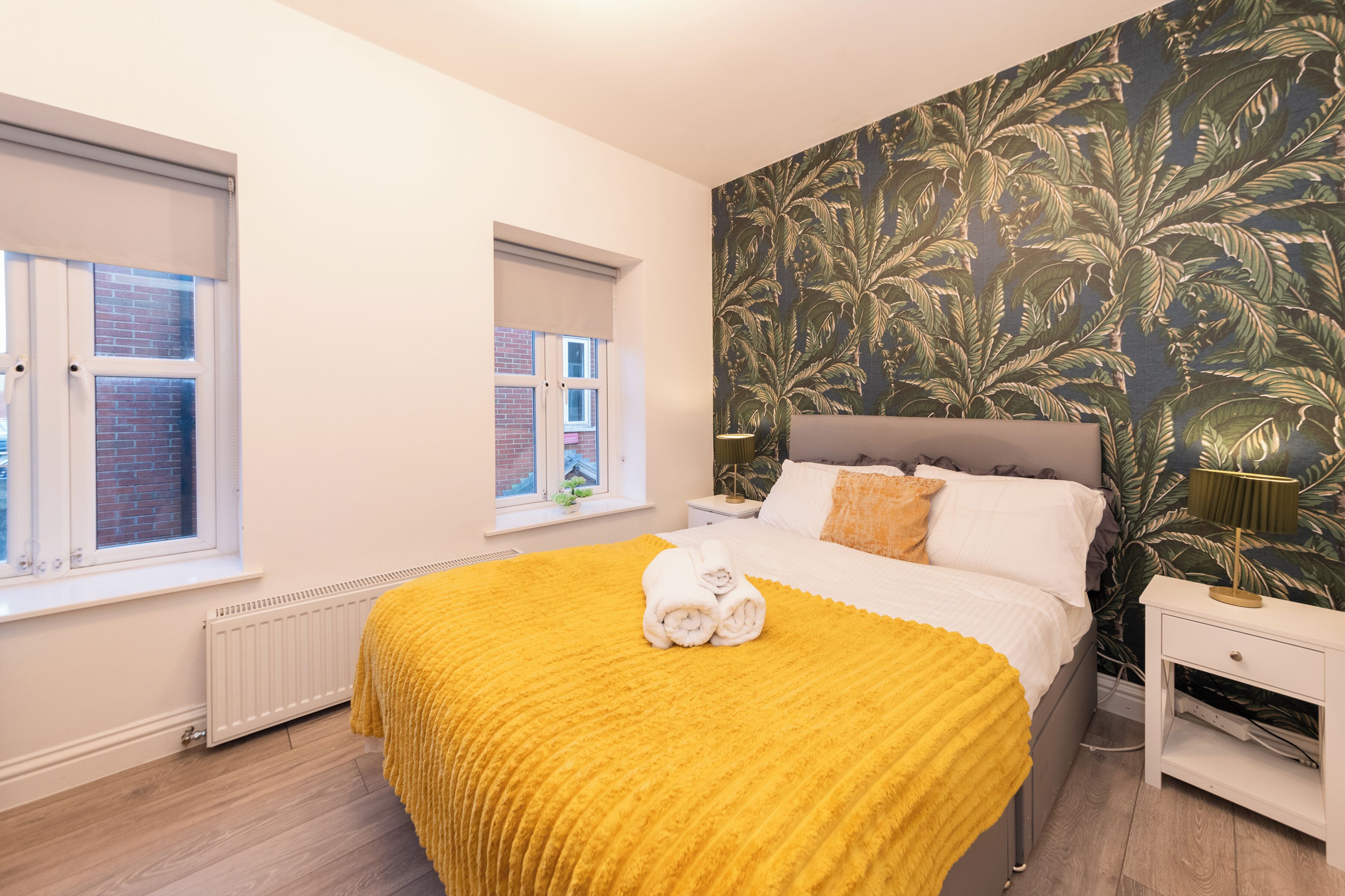 A bedroom with a bed, a nightstand, a lamp, and a window with a view of a brick building.
