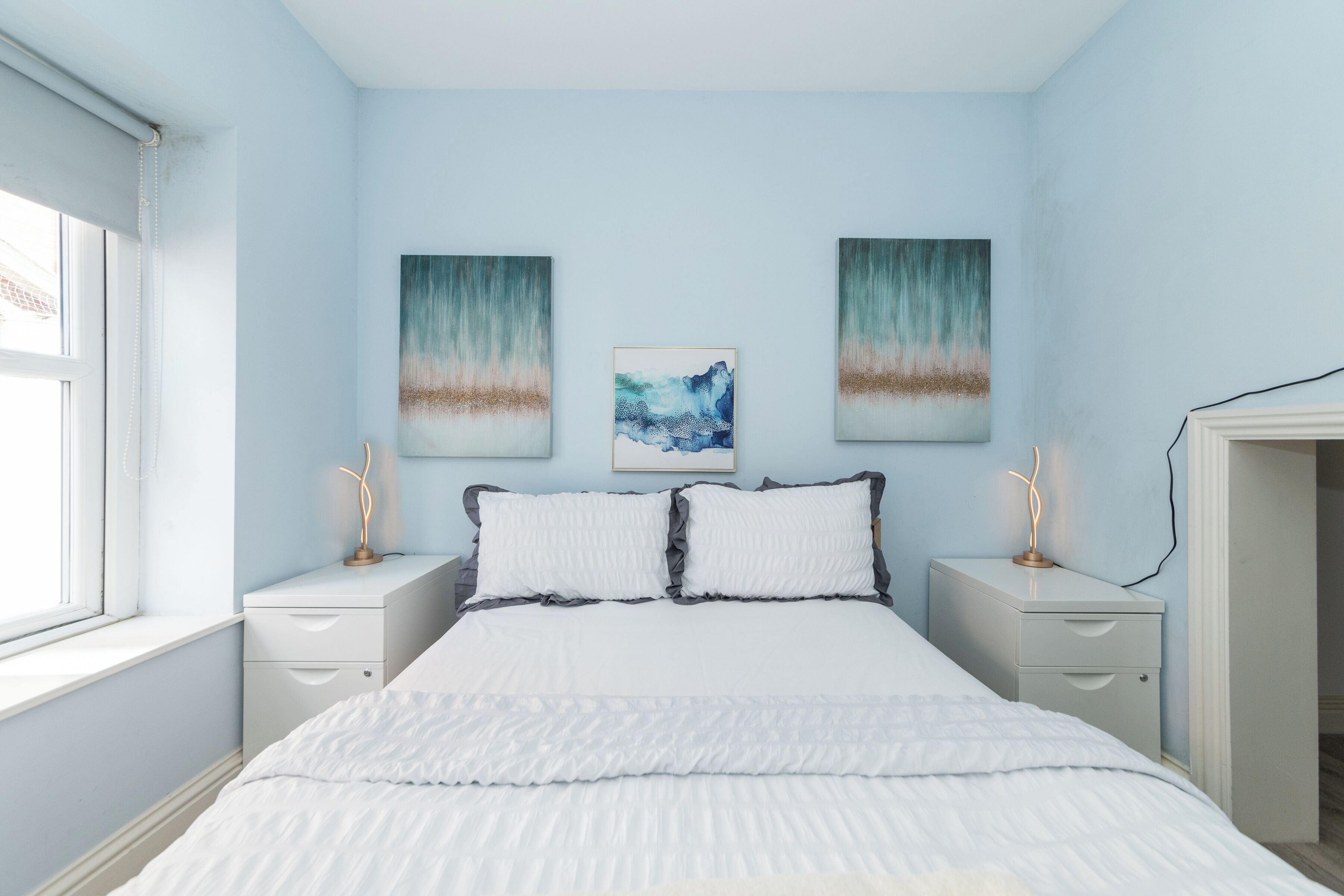 A bedroom with a bed, two bedside tables, and three wall-mounted paintings.