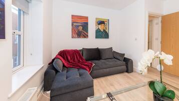 Een moderne woonkamer met een grijze modulaire bank, een rode plaid en twee schilderijen aan de muur.