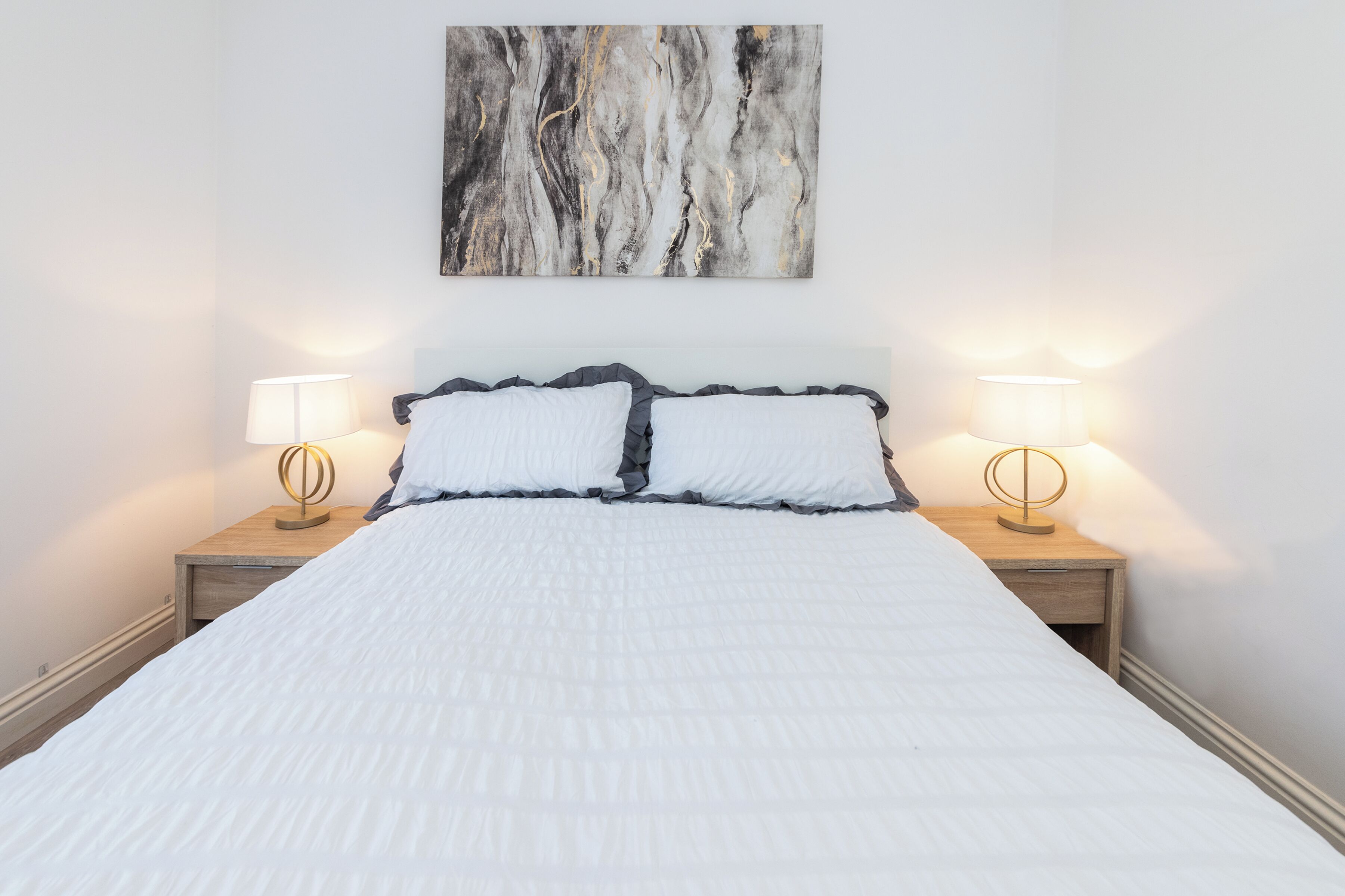 A bed with white bedding, two bedside lamps, and a wall-mounted abstract painting.