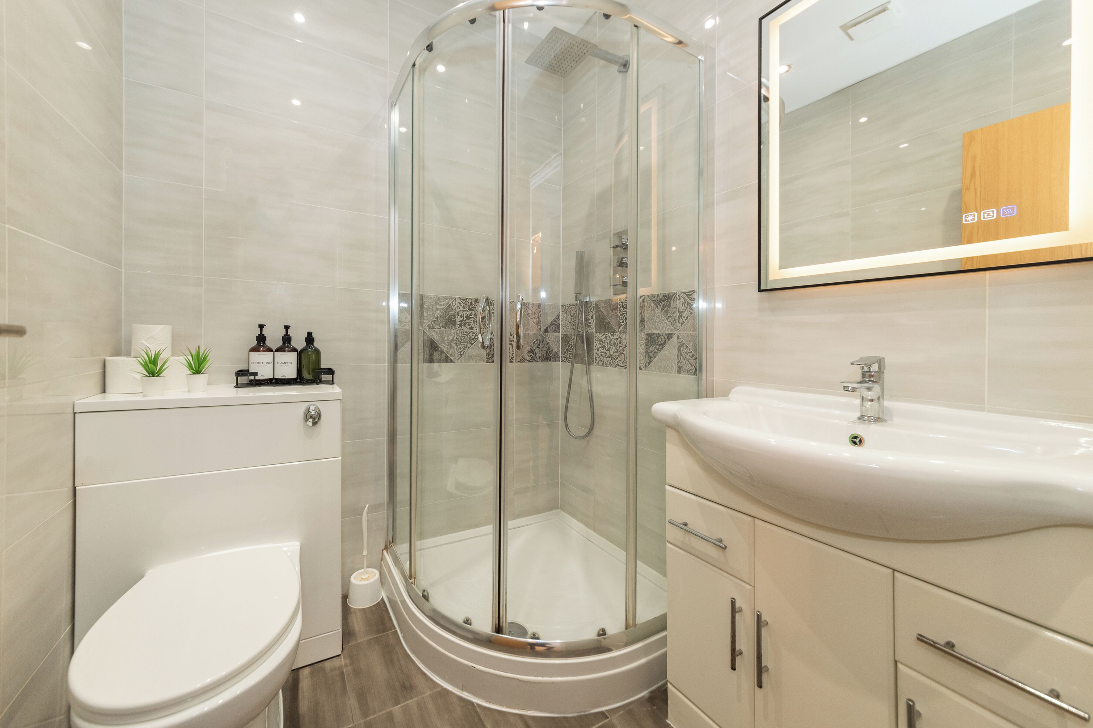 Un baño moderno con ducha de vidrio, inodoro blanco y lavamanos con espejo superior.