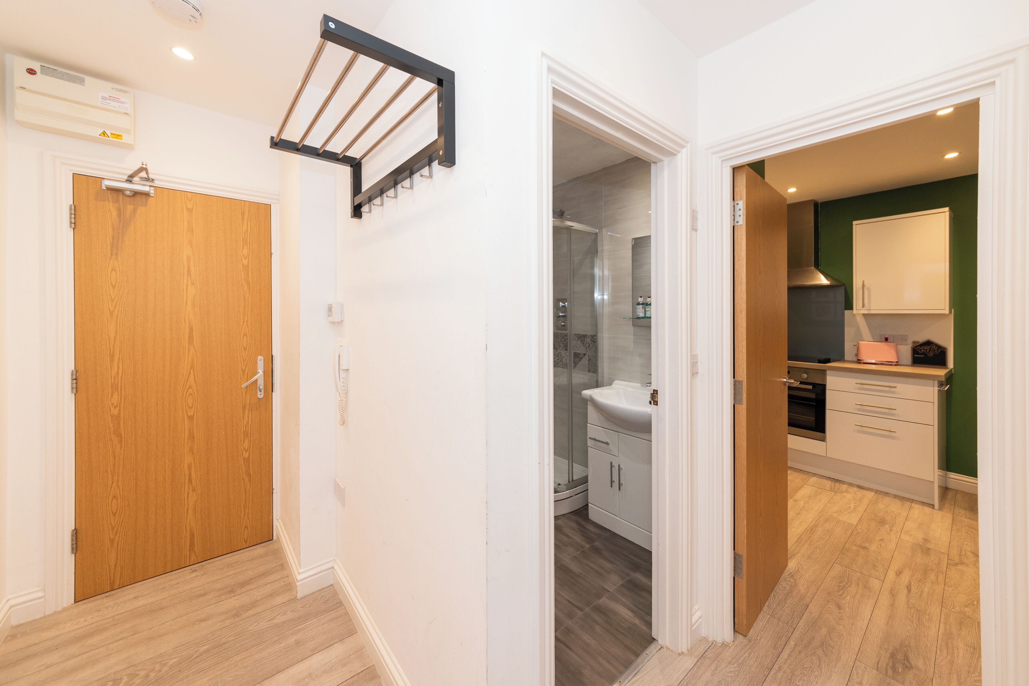 Un pasillo con puerta de madera, un perchero y un baño con ducha y lavamanos.