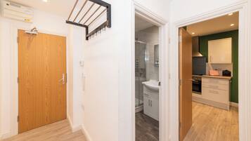 Un pasillo con puerta de madera, un perchero y un baño con ducha y lavamanos.