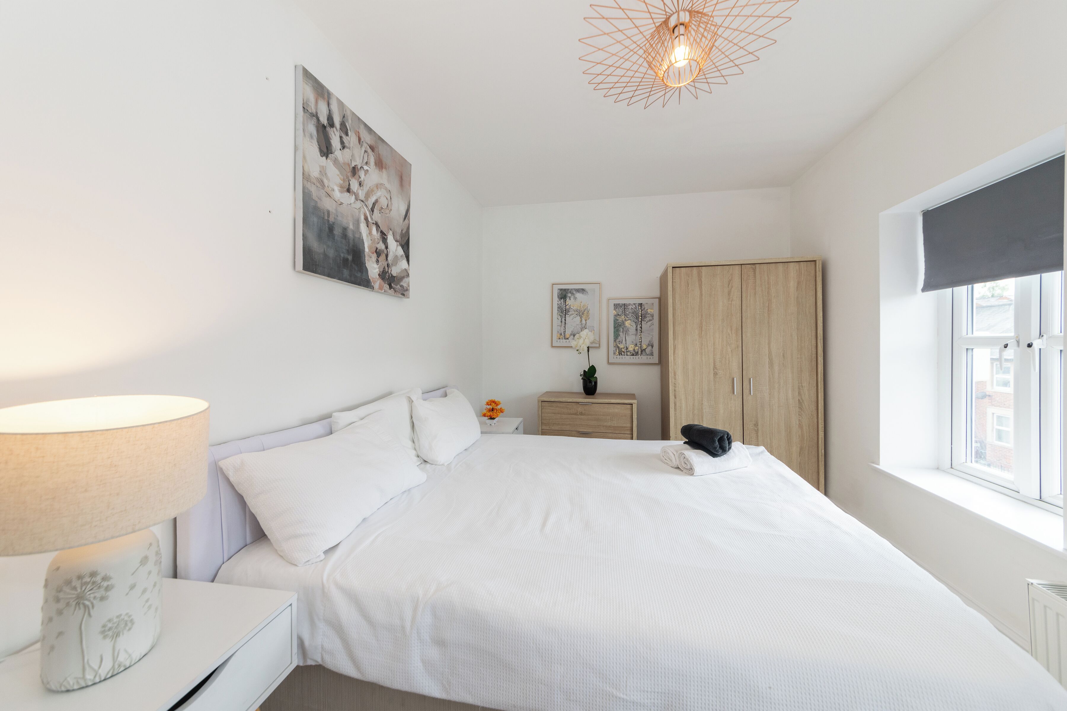 A bedroom with a bed, a bedside table with a lamp, a wardrobe, and a window with a view.