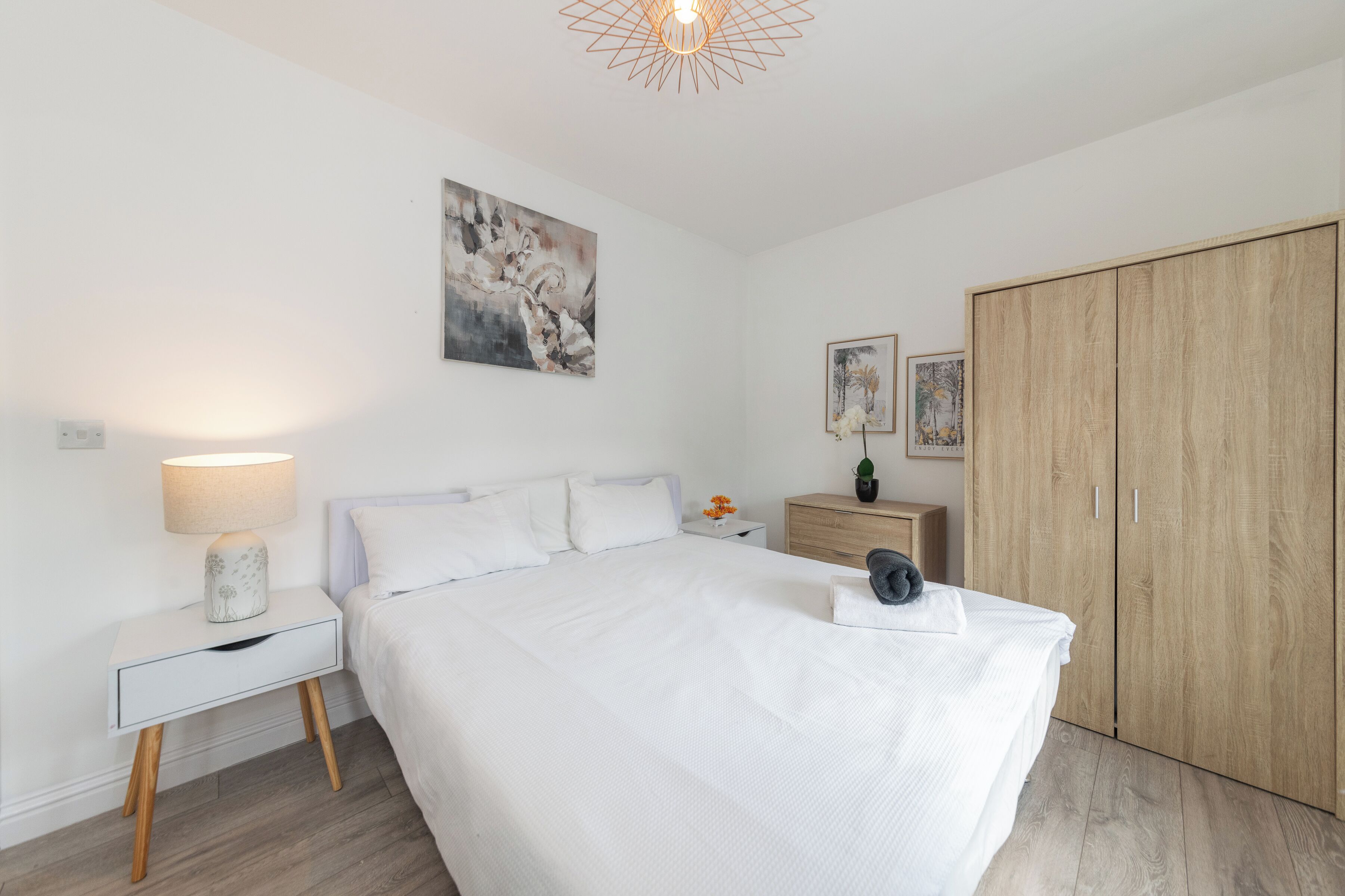 A bedroom with a bed, bedside tables, a wardrobe, and artwork on the walls.