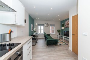 Una cocina moderna con estufa integrada, un comedor con sofá verde y un televisor en la sala.