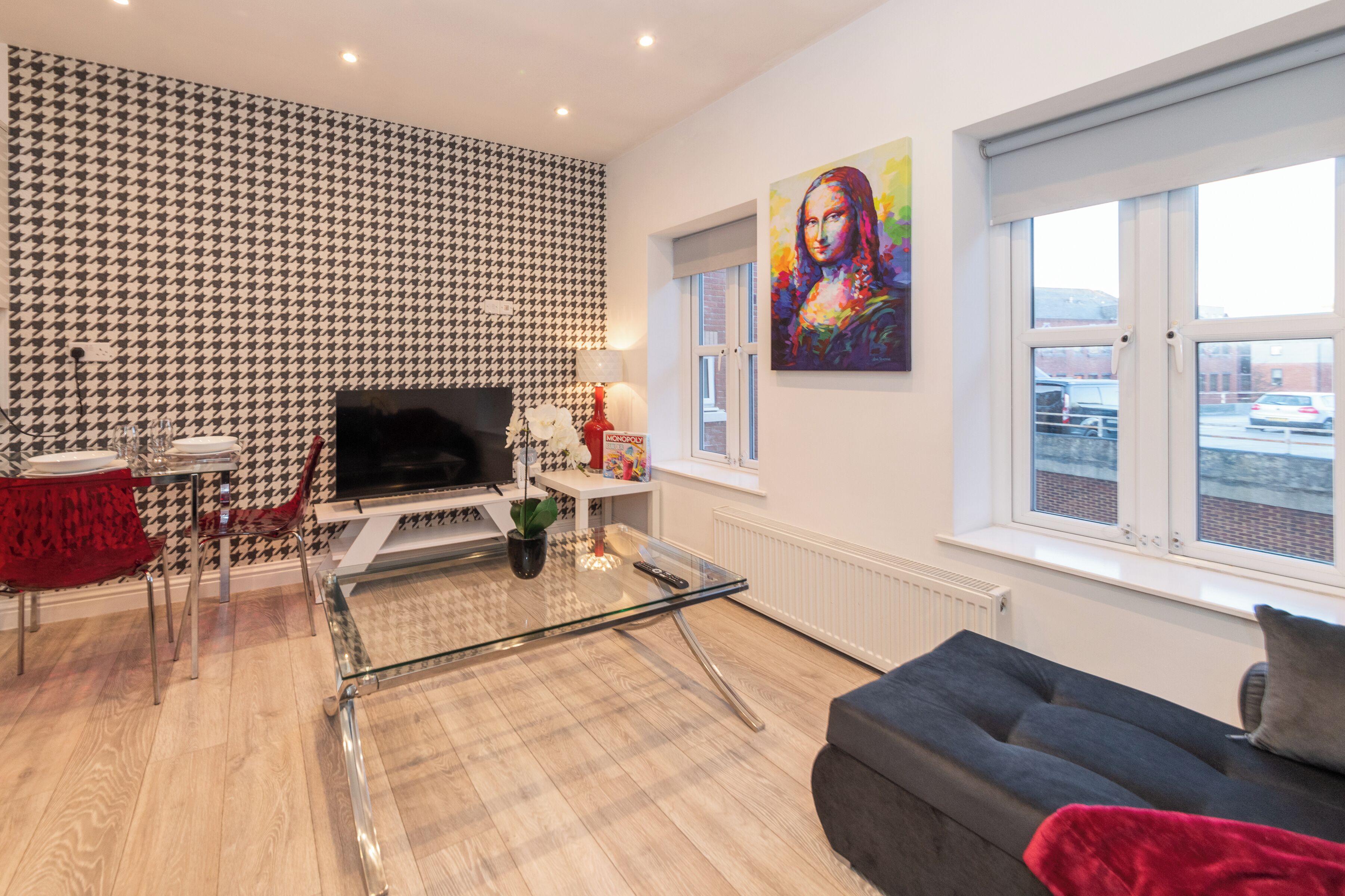 Un salon moderne avec un mur orné d’un motif à carreaux, une table basse en verre, un canapé gris et une grande fenêtre offrant une vue dégagée.