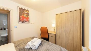 A hotel room with a bed, a desk, a chair, a wardrobe, a bathroom with a toilet, and a poster on the wall.