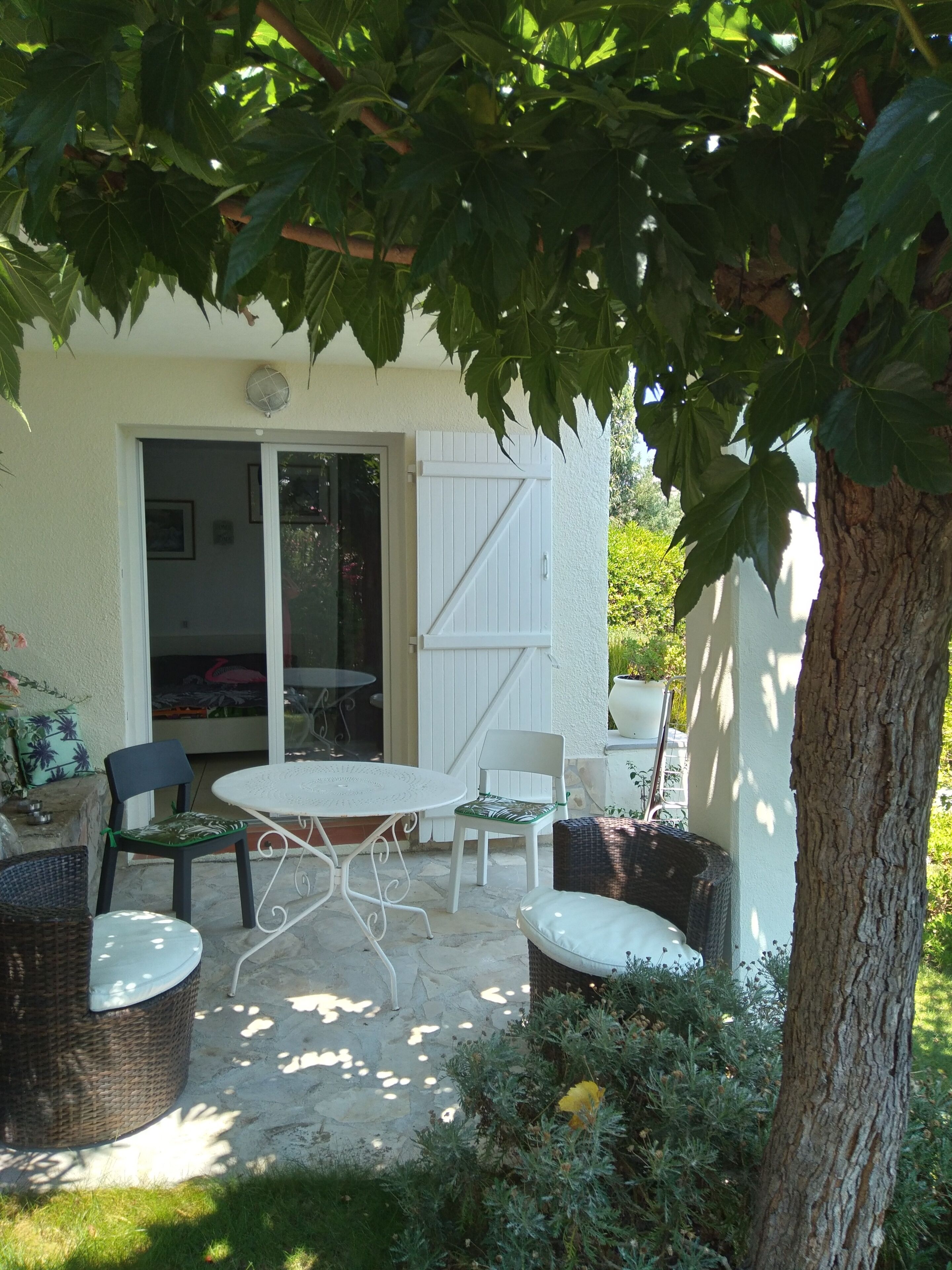 An outdoor patio with a table and chairs, a covered seating area, and a tree providing shade.