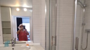 Et badeværelse med et glasvægshus, en vask med spejl og en kommode med skuffer.