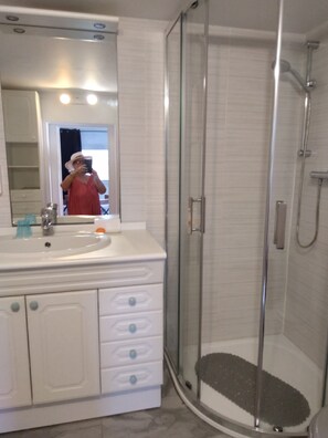 Ein Badezimmer mit einer Duschkabine, einem Waschbecken mit Spiegel und einem Schminktisch mit Schubladen.