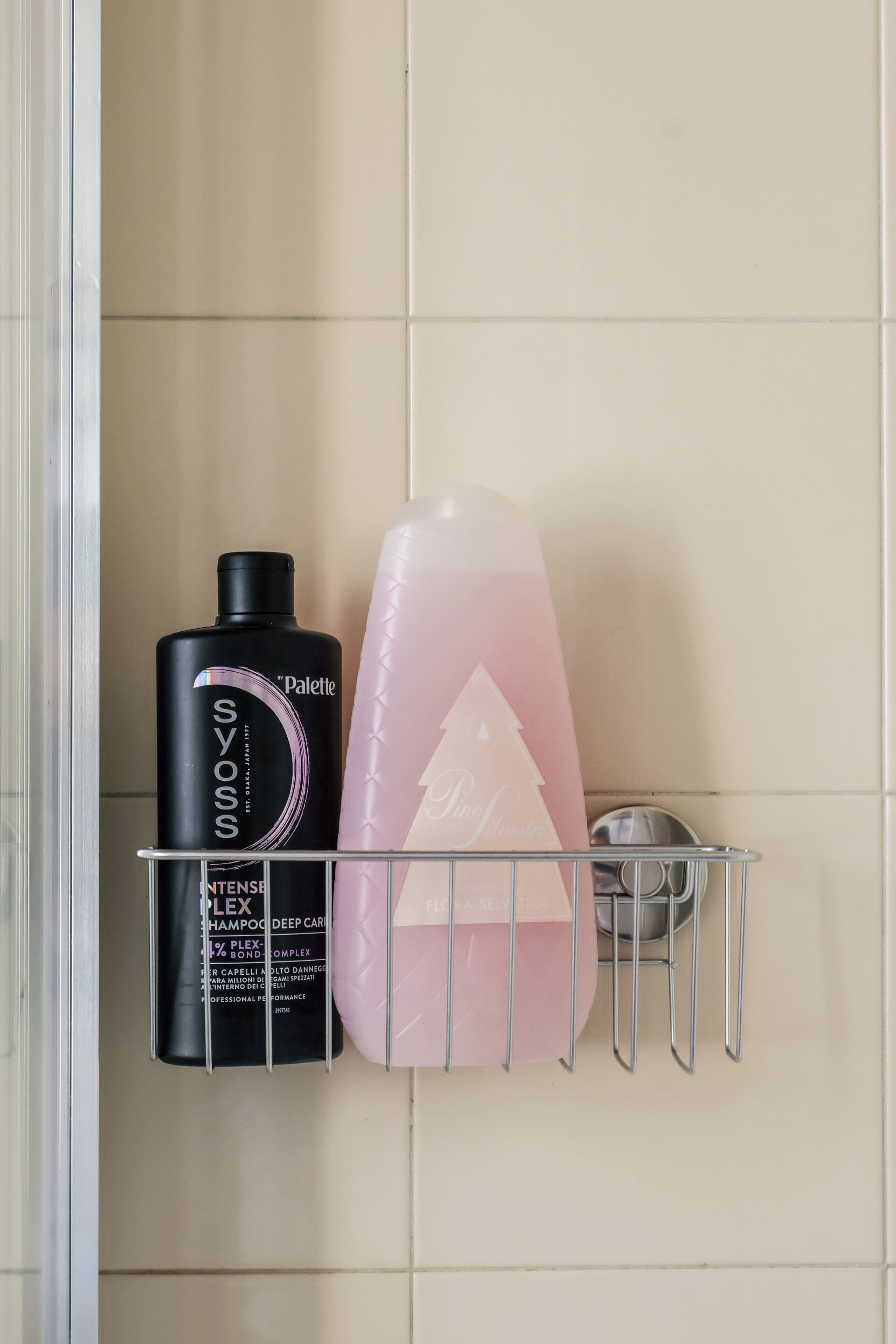 Une étagère de salle de bain avec un flacon noir contenant un produit capillaire et un flacon rose contenant une lotion pour le corps.