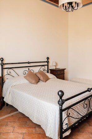 A bed with a white quilt, two pillows, a nightstand with a lamp, and a ceiling light fixture. - La Casa sul Corso - Nel cuore di Foiano della Chiana (Foiano della Chiana)