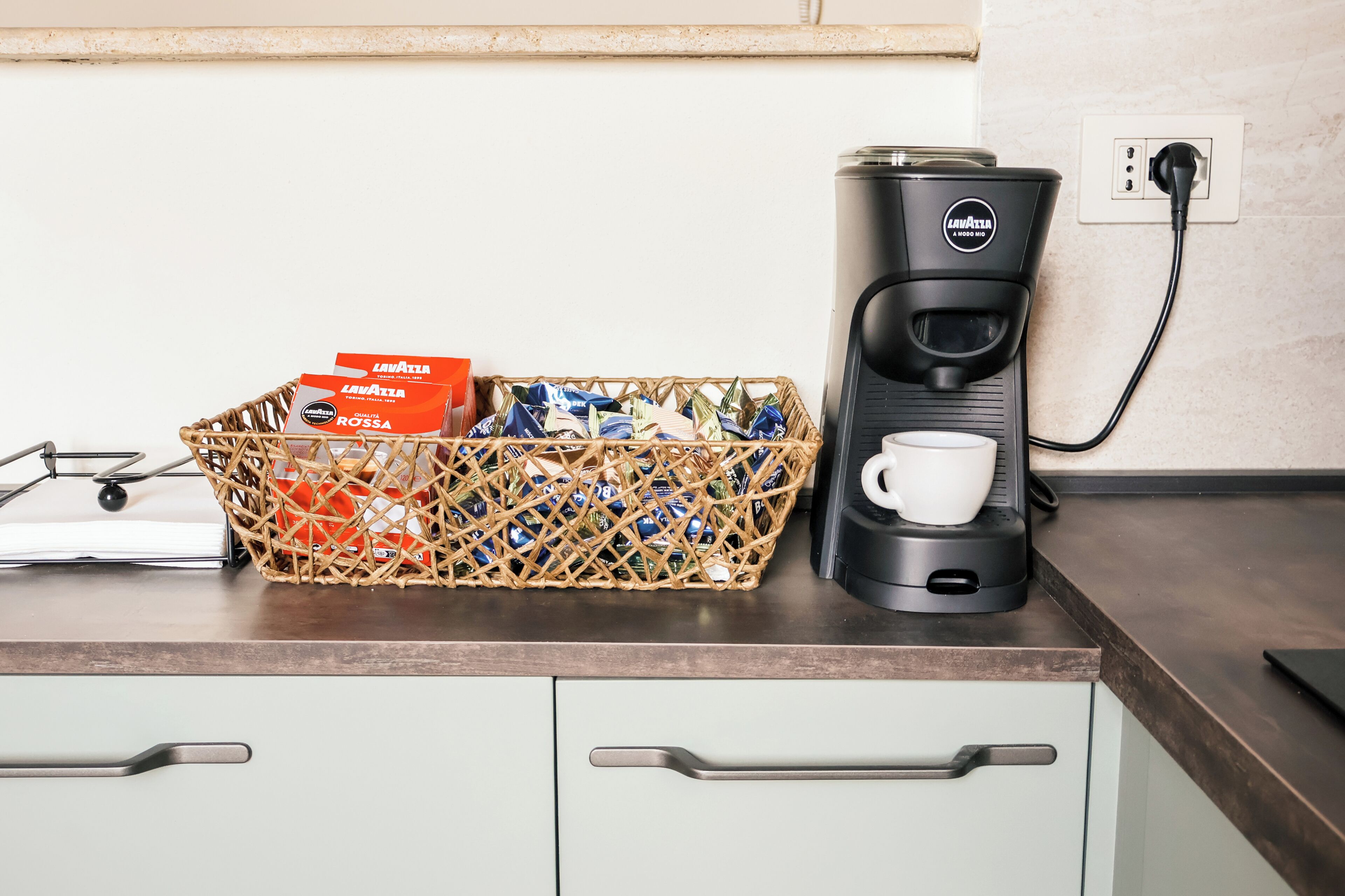 Un comptoir de cuisine avec une machine à café, un panier de bouteilles d’eau et une boîte de capsules de café.