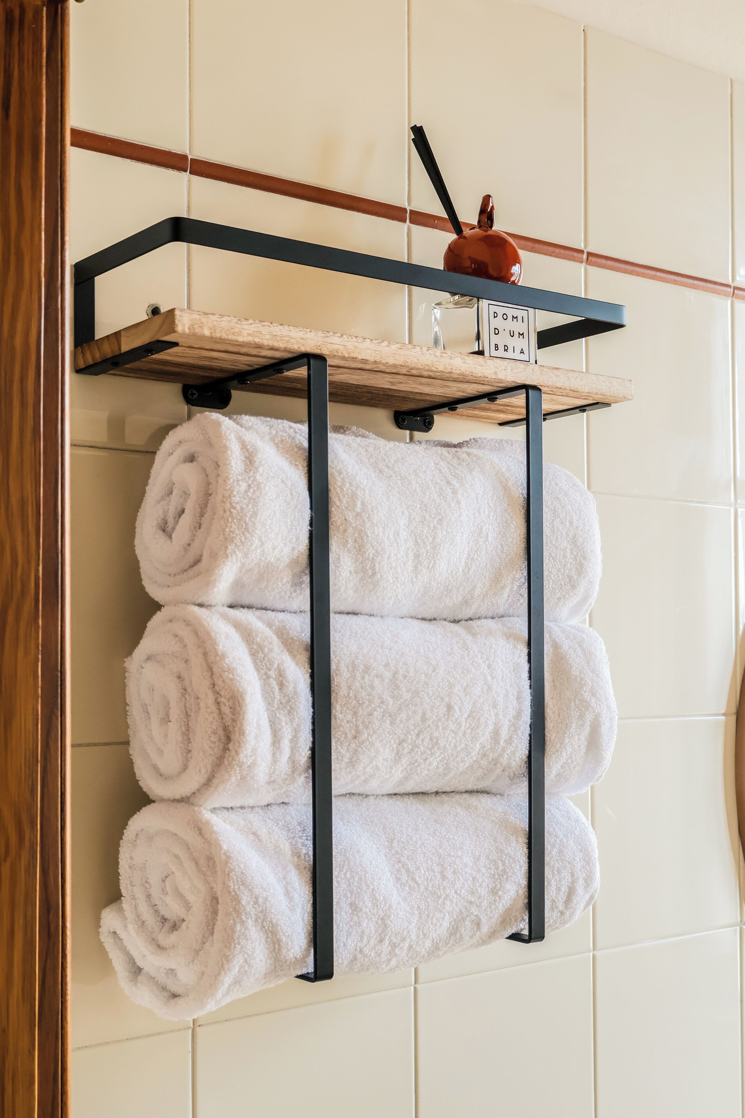 Une salle de bain avec un porte-serviettes où sont rangées des serviettes pliées et une petite étagère sur laquelle est posé un objet décoratif.