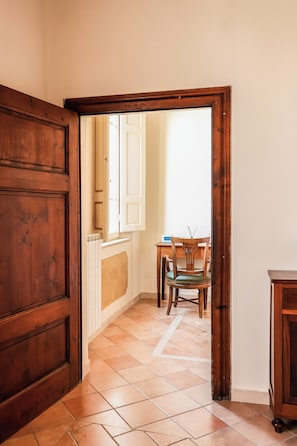 Un pasillo con una puerta de madera, un radiador, una silla de madera y una pequeña mesa.