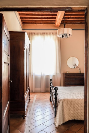 Une chambre à coucher avec un lit, une commode, un miroir et une fenêtre avec des rideaux.