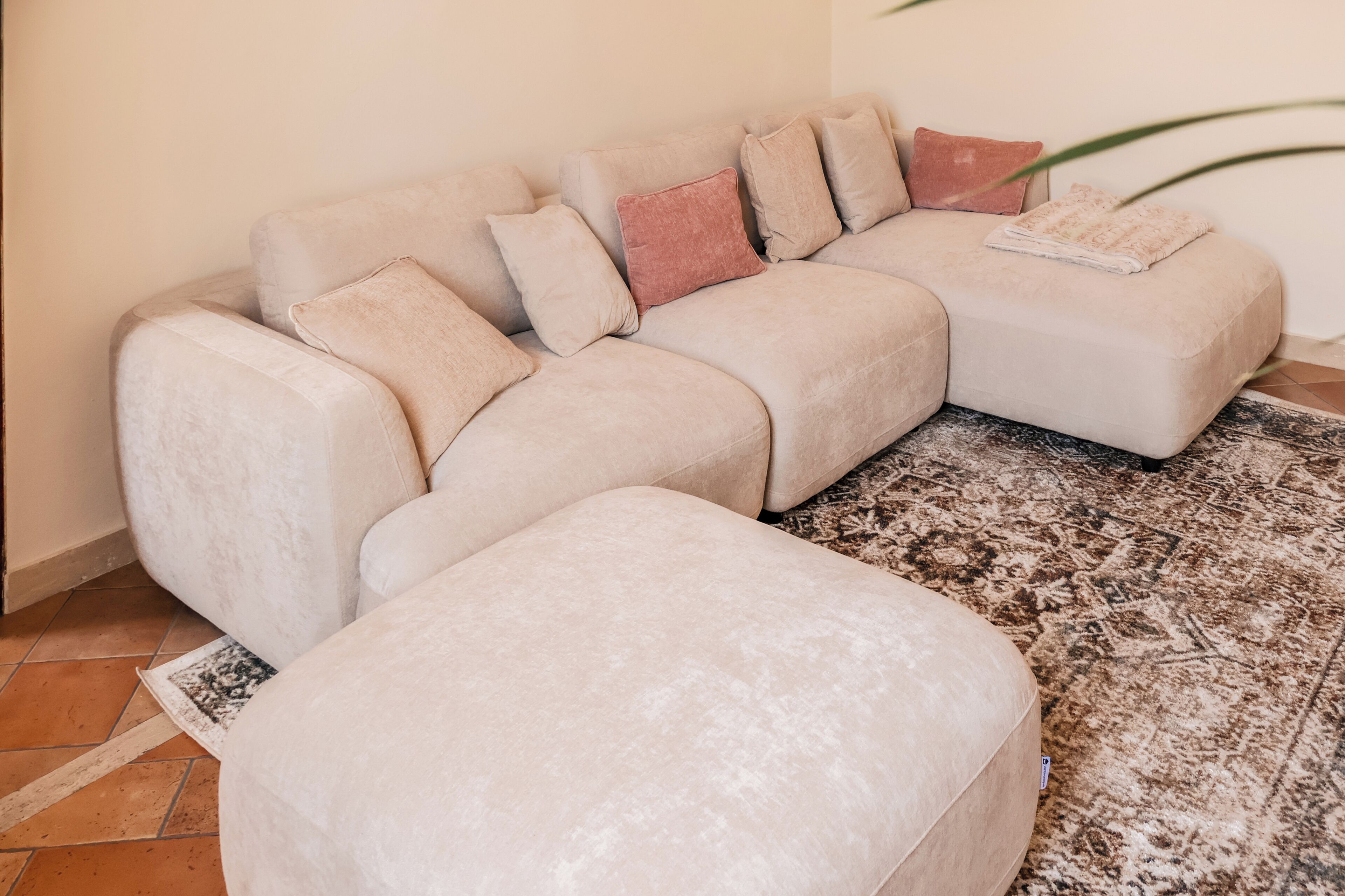 Un canapé modulable doté de plusieurs coussins et accompagné d’un pouf assorti, le tout posé sur un tapis à motifs.