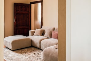 A corner room with a wooden door, a beige sofa with cushions, and a patterned rug. - La Casa sul Corso - Nel cuore di Foiano della Chiana (Foiano della Chiana)