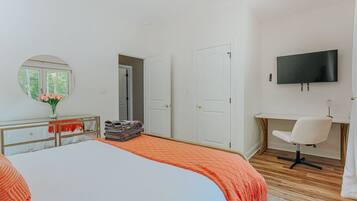 A bedroom with a bed, a desk, a chair, a TV, and a mirror.
