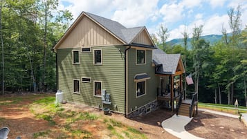 A two-story house with a porch, a flag, and a view of trees and mountains.
