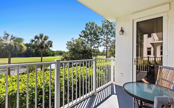 Ein Balkon mit Glastisch und Stühlen, einem weißen Geländer und Blick auf einen Golfplatz und Bäume.