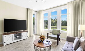 A living room with a flat-screen TV, a coffee table with a vase of flowers, a sofa, and a chair. - Fairway Views & Resort in Sandestin's Baytowne Wharf (Miramar Beach)