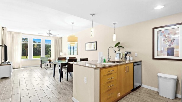 Een moderne keuken met een centraal eiland, een eethoek met een tafel en stoelen, en uitzicht op de omgeving door grote ramen.