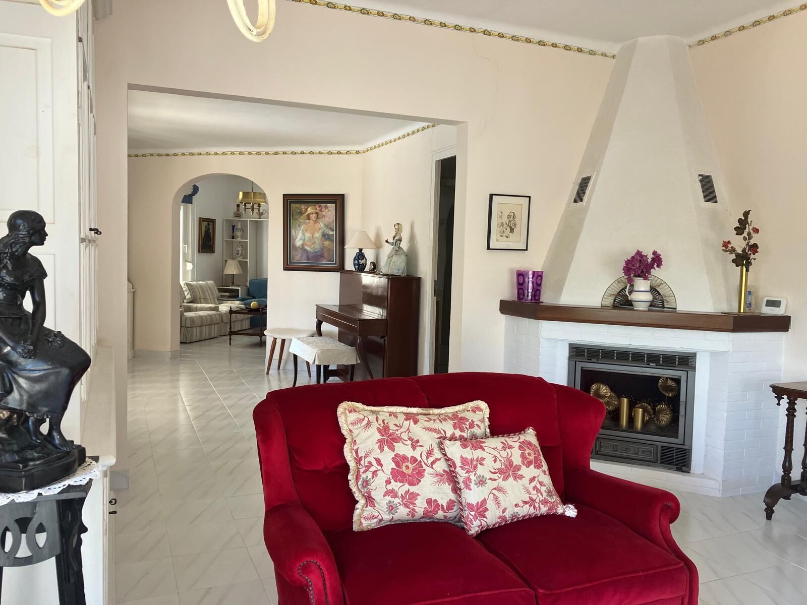 Un salon avec un canapé rouge, une cheminée et une statue.