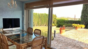 Uma sala de jantar com mesa de vidro, cadeiras de vime e um lustre moderno.