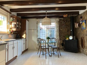 A kitchen with a dining area, wooden beams, a stone wall, and a view through a window. - Elegant villa with a pool and panoramic views in Ságaró, Costa Brava. (Castell d'Aro)