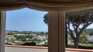 A view from a window with a curtain, overlooking a residential area with houses, trees, and a clear sky. - Elegant villa with a pool and panoramic views in Ságaró, Costa Brava. (Castell d'Aro)