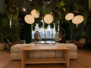 A modern lounge with a sofa, round tables, hanging planters, and a view of the city. - Downtown Miami Boutique Residence with Rooftop Pool, Gym, Cowork & Den (Miami)