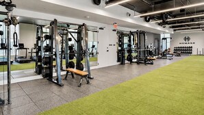 A gym with weightlifting equipment, a green carpeted area, and a wall with a logo. - Downtown Miami Boutique Residence with Rooftop Pool, Gym, Cowork & Den (Miami)