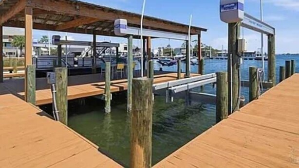 A wooden dock extending into a body of water with a covered seating area and a signpost. - Relaxing, water front rental in Orange Beach with pool access and boat slip. (Orange Beach)