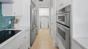 A narrow kitchen with white cabinets, a black countertop, and stainless steel appliances. - Relaxing, water front rental in Orange Beach with pool access and boat slip. (Orange Beach)