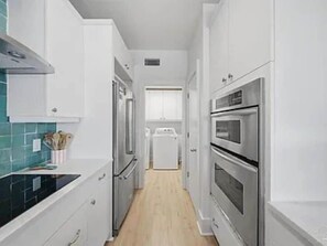 A narrow kitchen with white cabinets, a black countertop, and stainless steel appliances. - Relaxing, water front rental in Orange Beach with pool access and boat slip. (Orange Beach)