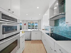 A modern kitchen with white cabinetry, a built-in oven, a stove, and a backsplash with blue tiles. - Bayou Breeze Unit 2 (Orange Beach)