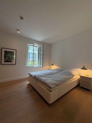 Ein Schlafzimmer mit einem Bett, zwei Nachttischen, einem Fenster und einem gerahmten Bild an der Wand.