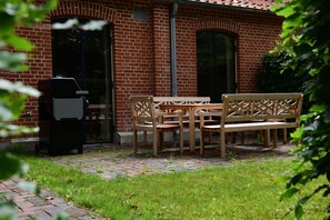 A brick building with a patio area featuring a wooden table and chairs, a grill, and a grassy lawn. - Exclusive "Backbord" vacation rental with private boat access and dock (Boren)