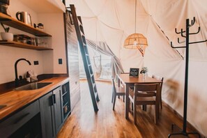 A tented accommodation with a wooden dining table, chairs, a hanging light fixture, and a ladder. - Ananta Forest (Monteverde)