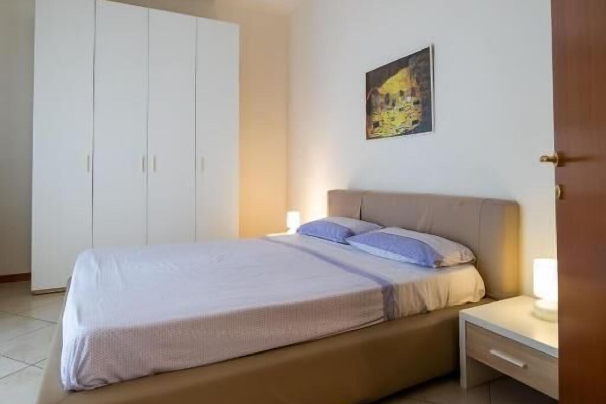 A bedroom with a bed, bedside tables, a wardrobe, and a painting on the wall.