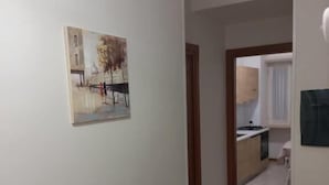 A hallway with a painting, a kitchen area, and a door leading to another room. - Le Gemme Appartamenti  (Napoli)