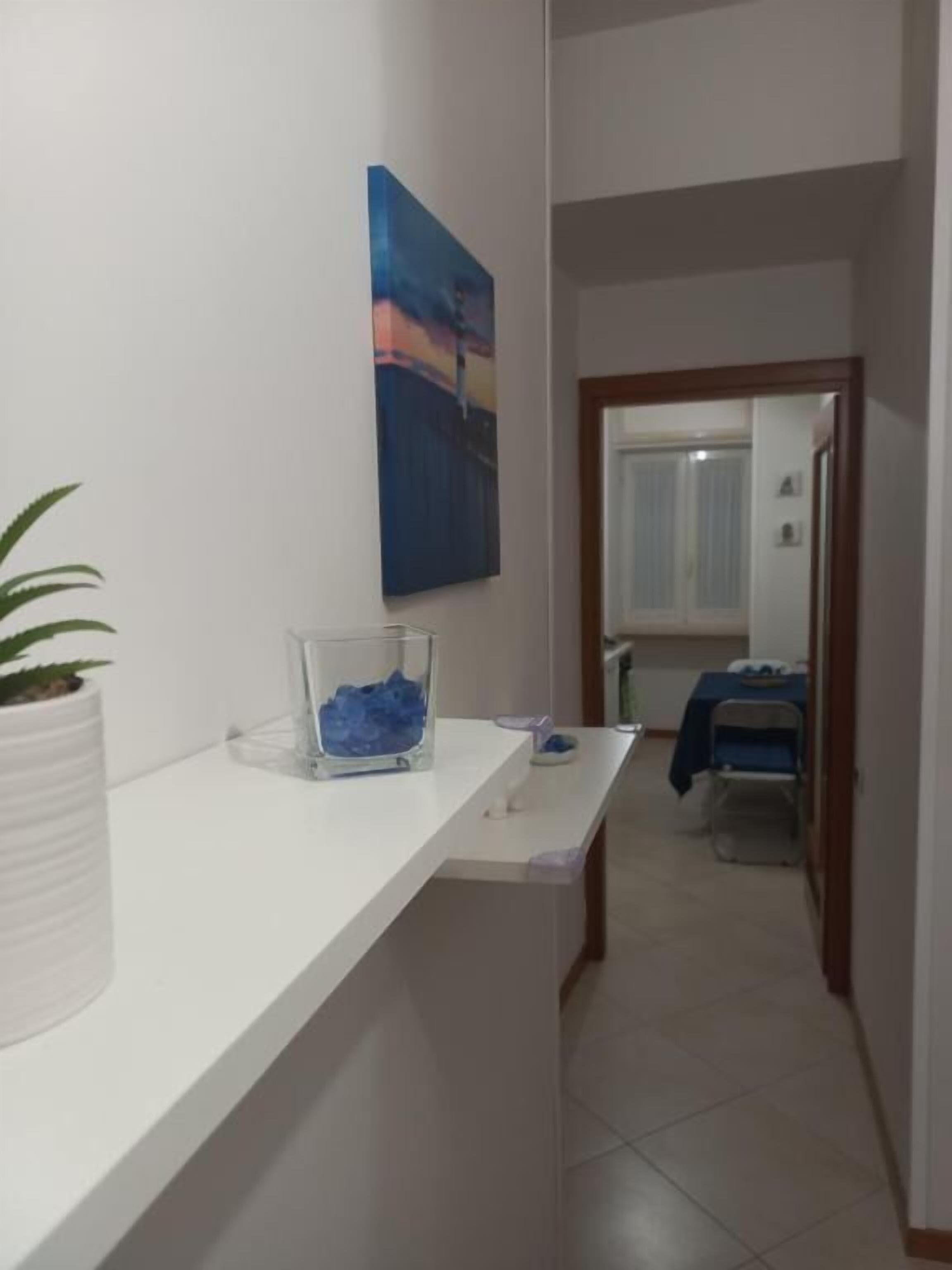 A hallway with a white counter, a potted plant, and a blue abstract painting on the wall.