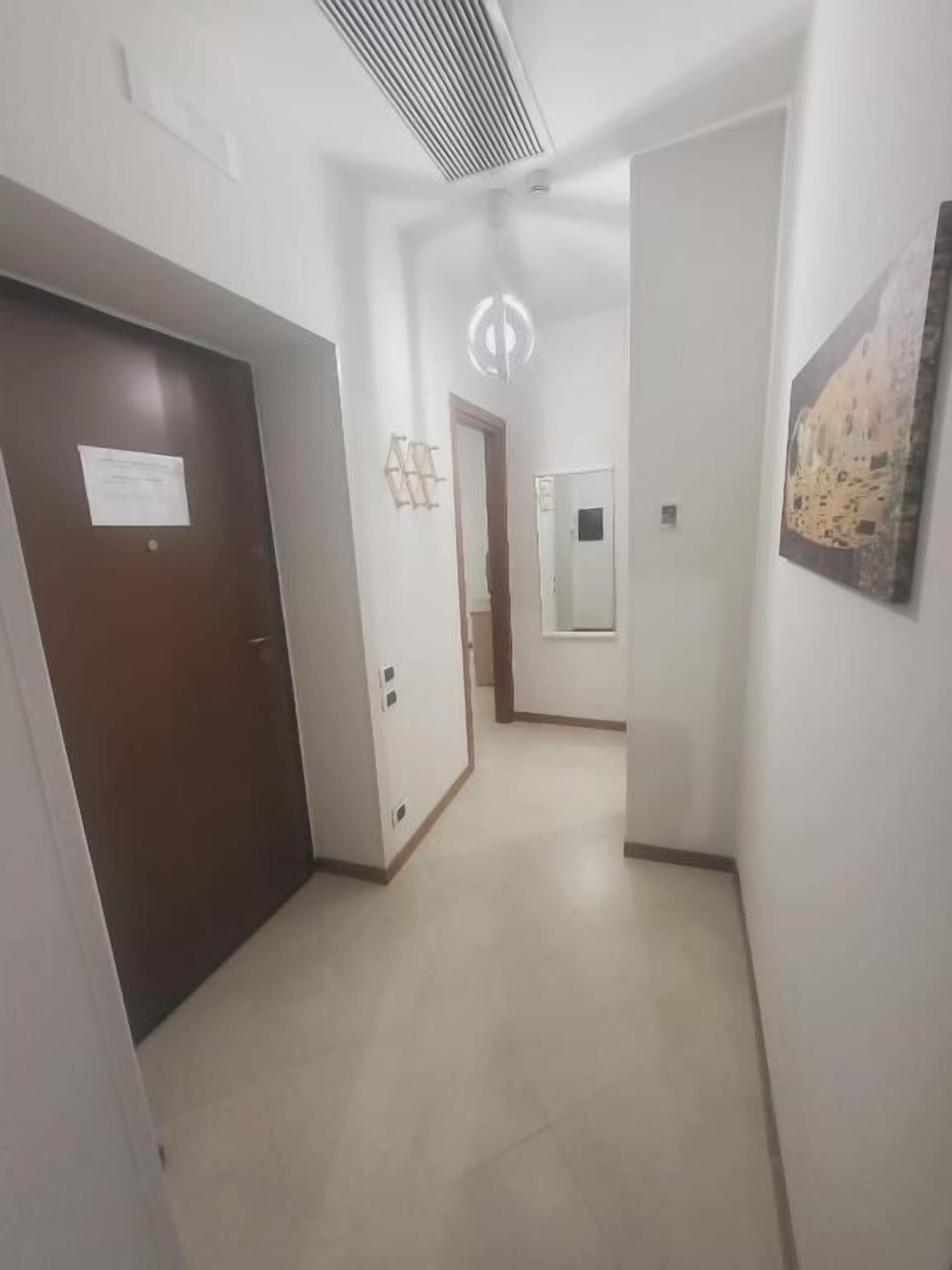 Un passadís amb una porta a l'esquerra, un lluminari al centre i un quadre amb marc a la paret dreta.