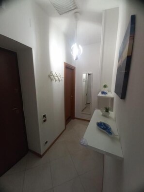 A hallway with a door, a light fixture, a small plant, and a mirror.