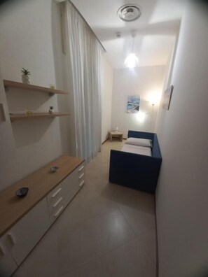 Una habitación pequeña con cama, mesita de noche y una ventana con cortinas.