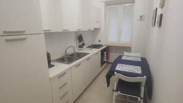 A compact kitchen with white cabinets, a small dining table, and a window with curtains.